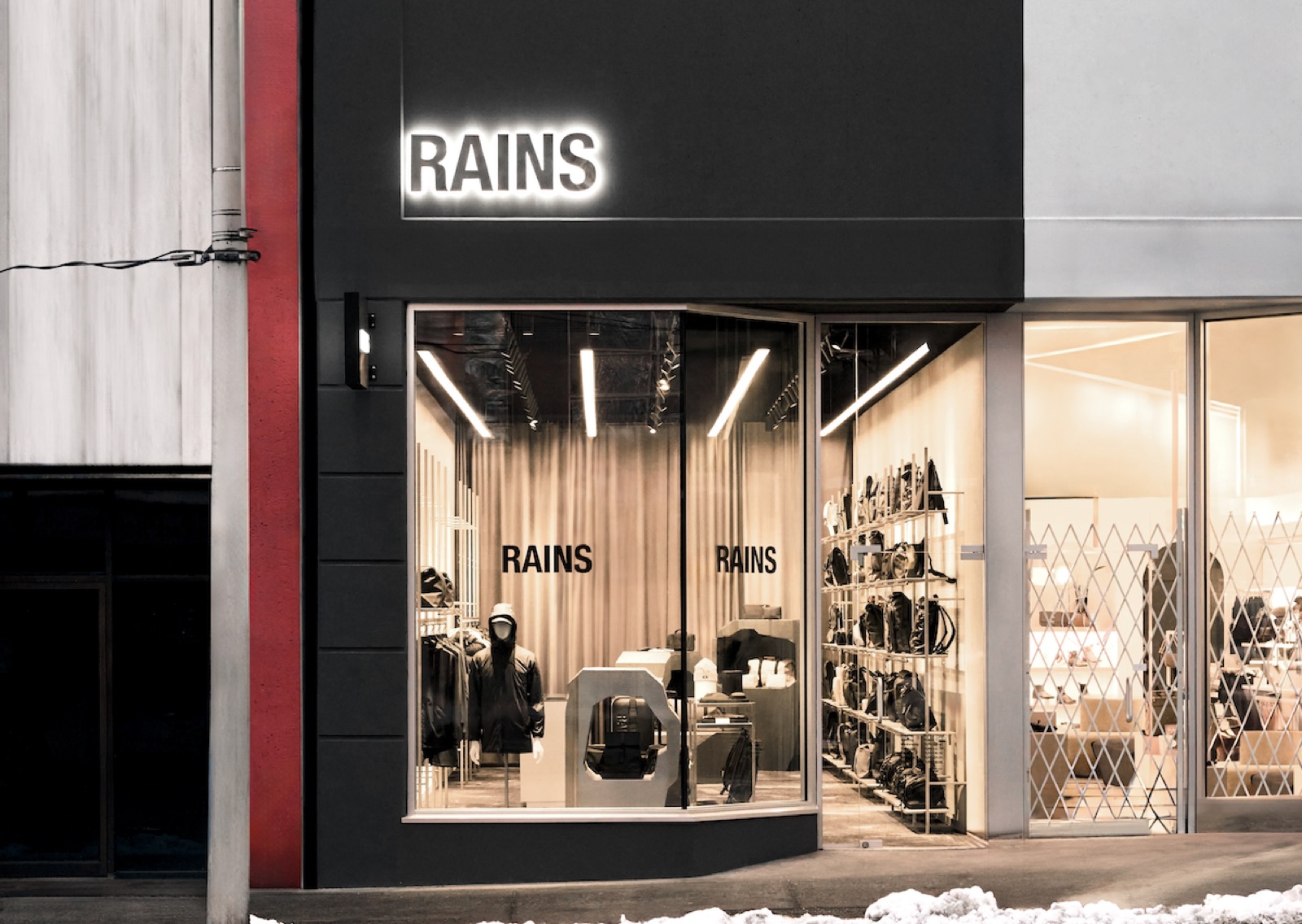The RAINS store on West 4th, Vancouver, at dusk — glowing sign and warm-lit interior, designed, built and operated by Readymade